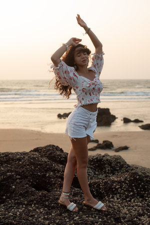 Portrait of young Asian woman standing on stones near beach, raising hands with closed eyes, enjoying holiday. Beauty.の写真素材