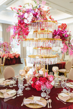 Crystal high stand with bright floral arrangement in red tones in middle of round table set.の写真素材