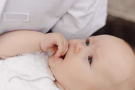 Top view of serious charming newborn girl in white dress, held in arms of unrecognizable parent.の写真素材