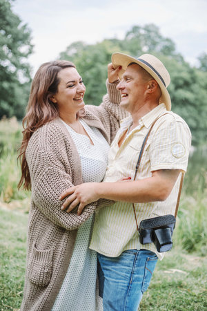 Happy together. Beautiful smiling woman in long knitted cozy cardigan hugs her husband in nature.の写真素材