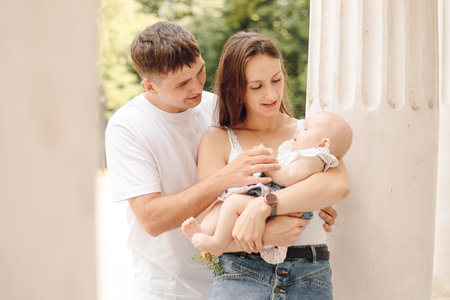 Life insurance. Young family on sunny day in nature, mom holds tiny baby in her arms, dad hugs themの写真素材