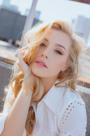 Close-up portrait of charming blonde in white romantic dress, with long wavy loose hair on summer day in city .の写真素材