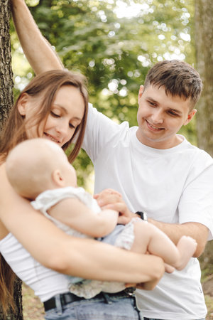Vertical family portrait. Happy parents admire their baby in arms of their mother on summer.の写真素材