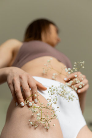 Bottom view. Delicate flower of gypsophila is pressed against tanned healthy skin of female body in sports underwear.の写真素材