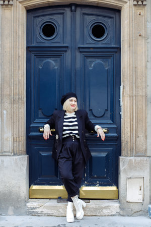 Full-length vertical portrait of stylish blonde standing with her back to blue door. Urban style.