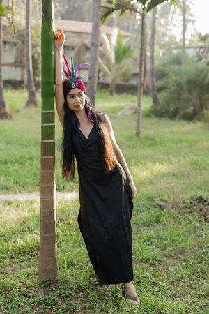 Harmony, self-search. Brunette i nfeathered headdress greets dawn of sun, leaning against to tree.の写真素材