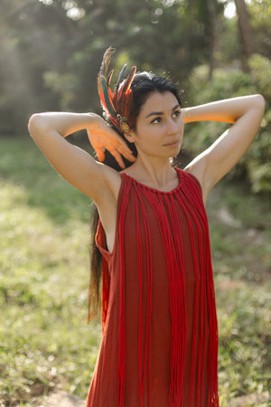 Lovely brunette with loose hair in red dress with stylized Indian feather decoration greets dawn.の写真素材