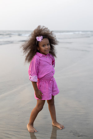 Full-length portrait of African-American girl with curly hair, enjoying sea, standing on seashore.の写真素材