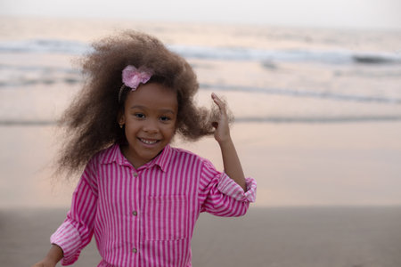 Portrait of charming happy African-American girl on sandy beach, against background of sea, ocean.の写真素材