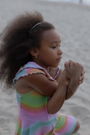 Childrens yoga. Charming African-American girl with curly hair on beach by sea on summer day.の写真素材