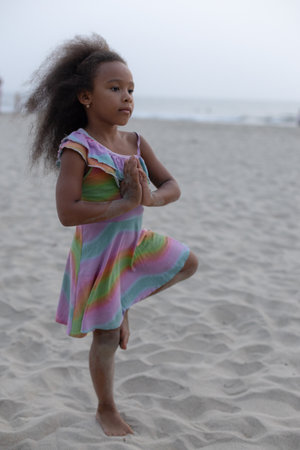 Full-length portrait of black girl who performs yoga balance exercise on beach in early morning.の写真素材