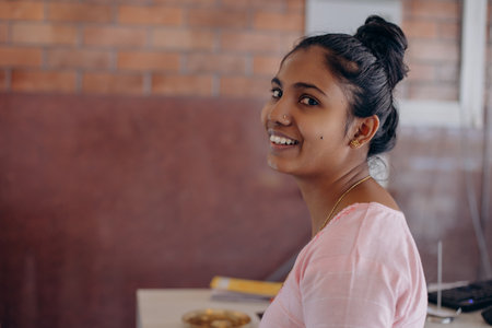 Portrait of charming young Indian woman in pink dress smiling at camera inside room. Positive.の写真素材