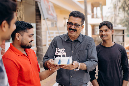 Group of four happy men. Man in shirt, glasses accepts birthday cake, congratulations from friendsの写真素材