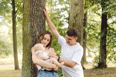 A couple holding a baby under a tree in the park, happy and enjoying natureの写真素材