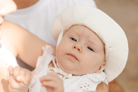 A happy baby in a white hat and dress, showcasing a cute fashion accessory