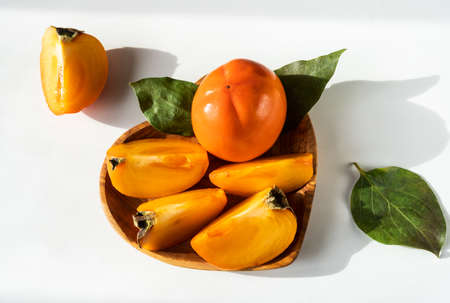 persimmon with slices, leaves in a wood plate on the white backgroundの写真素材