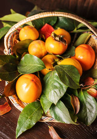 persimmon with leaves on the branches in a basket on the wooden backgroundの写真素材
