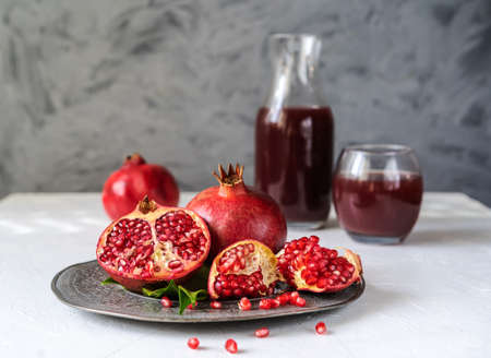 pomegranates on the plate with leaves, juice backside, grey background and white tableの写真素材