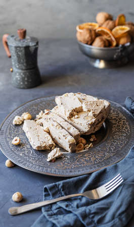 Halwa with hazelnuts, caffe pot, dry fruits, nuts, grey napkin, fork on grey background