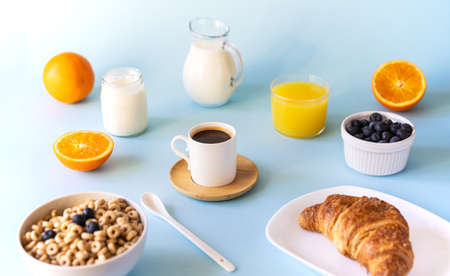 Breakfast concept with cup of coffee, croissant, wholegrain hoops, milk, orange juice, yogurt and blueberriesの写真素材