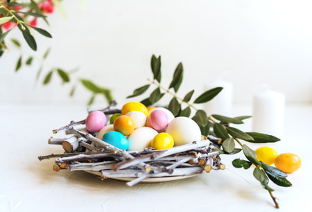 Holiday composition for Easter. Nest with coloured and white eggs, candles, olive branch and spring...