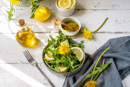 Dandelion salad with olive oil, lemon juice and spices on white wooden table with grey backgroundの写真素材