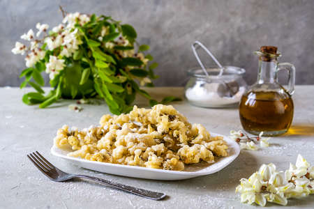 Acacia fried flowers or fritters on plate and on concrete background with fork, oil and sugar powderの写真素材