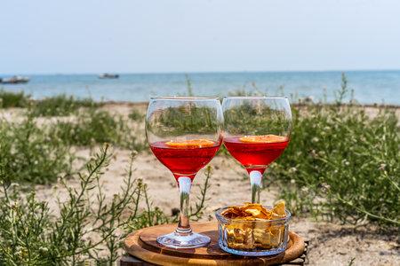 Two glasses of an Italian appetiser Gingerino drink with dry fruits snack on the beach with sea coast viewの写真素材
