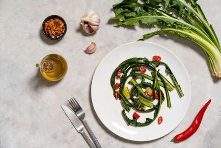 Chicory greens stewed with garlic and hot red paper on plate with ingredients. Top view with copy...