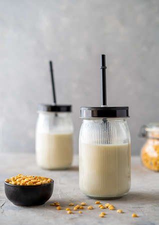 Vegan healthy pea milk in glass jars with drinking straws, concrete background, pea grains and...