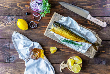 Smoked mackerel on wood stand, rings of onion, lemon, olives, olive oil, rosemary over wooden backgroundの写真素材