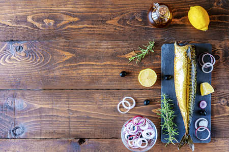 Smoked mackerel on stone cutting board, rings of onion, lemon, olives, olive oil, rosemary over wooden backgroundの写真素材