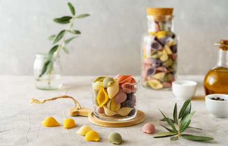 Multi-coloured Italian pasta conchiglie or seashells in glass and bottle, olive oil, salt, pepper,...