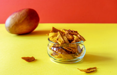 Mango chips in a glass jar over yellow and orange backgroundの写真素材