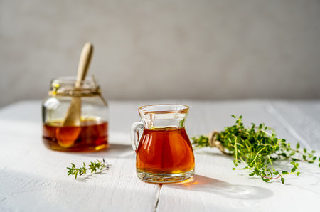 Thyme honey in small jug and jar, small thyme branch on white wooden table with grey backgroundの写真素材