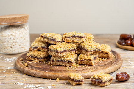 Homemade old fashioned date squares or Matrimonial bars on round wooden cutting board with ingredientsの写真素材
