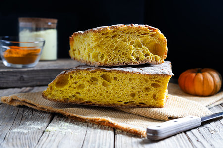 Turmeric bread on napkin, knife, flour and turmeric in powder on wooden table with dark background