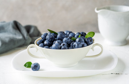 Fresh blueberries in a white teacup on the white wooden table with grey concrete background, closeup, free space for textの写真素材