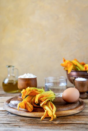 Zucchini flowers on a cutting board with basic ingredients to be fried in batter or make crepes. Wooden table, eggs, flour, olive oilの写真素材