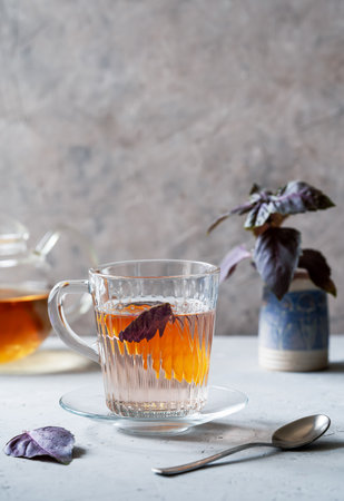 Healthy and immune boosty purple basil tea in a glass mugs with slice of orange and fresh leaves backside. Grey concrete background, vertical banner with space for textの写真素材
