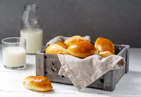 Baked homemade pies in the wooden grey box, milk in glass and bottle over white and grey backgroundの写真素材