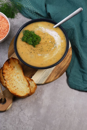 red lentils soup puree in dark bowl with bread on grey marble tableの写真素材