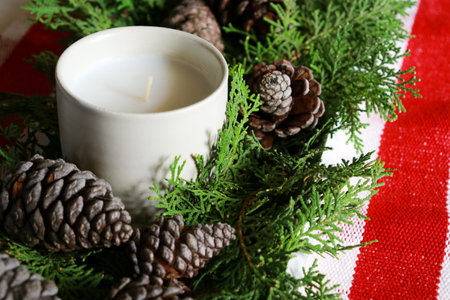 christmas composition with a candle, pine cones and green needles with red table runnerの写真素材