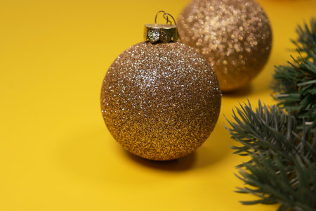 golden Christmas ornament balls on yellow background with green pine treeの写真素材