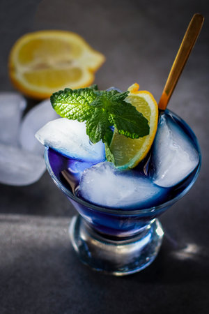 Close up of blue lagoon cocktail with ice, mint and lemon, grey background