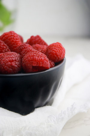 close up of fresh raspberries in dark bowl, blurred white background