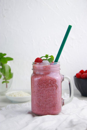 raspberry coconut smoothie with ice in a jar with straw, white background