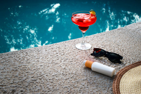 refreshing red Cocktail at the pool with sunscreen, sunglasses and straw hatの写真素材