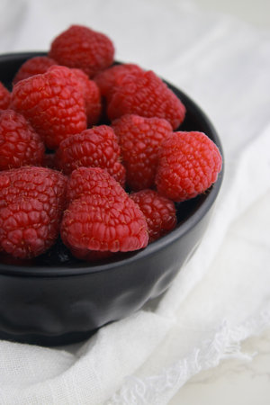 close up of fresh raspberries in dark bowl, blurred white background