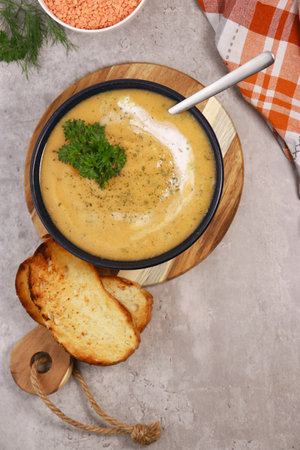 red lentils soup puree in dark bowl with bread on grey marble tableの写真素材